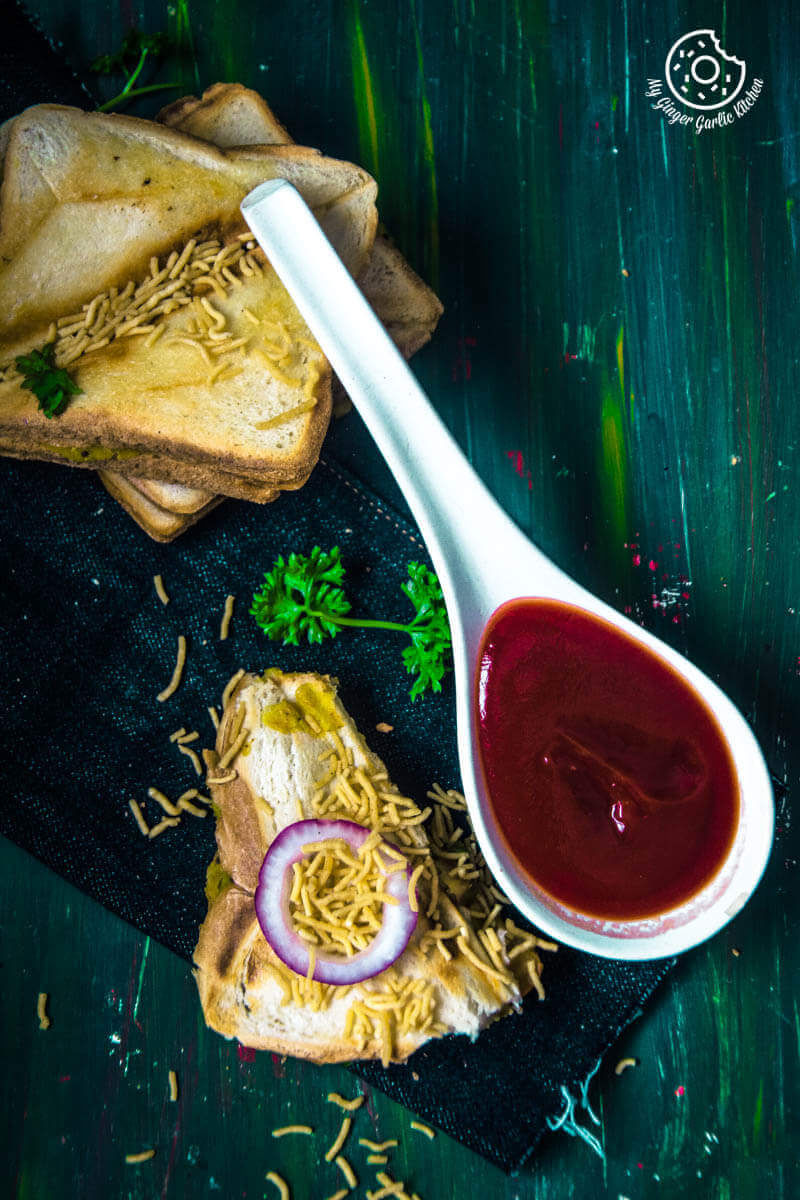 a spoon with some tomato ketchup on it next to Bomabay masala toast topped with onion and sev