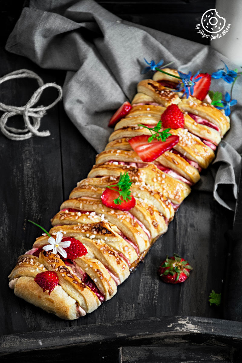 a close up of a braided strawberry cream cheese pastry with strawberries and other toppings