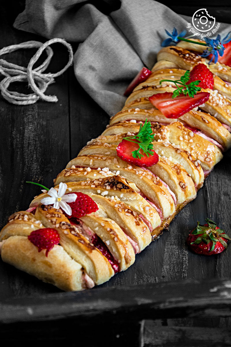 braided strawberry cream cheese pastry with strawberries and nuts on a wooden table