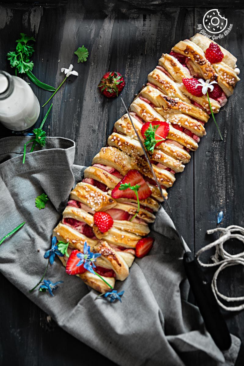 a long braided strawberry cream cheese pastry with strawberries and flowers on it