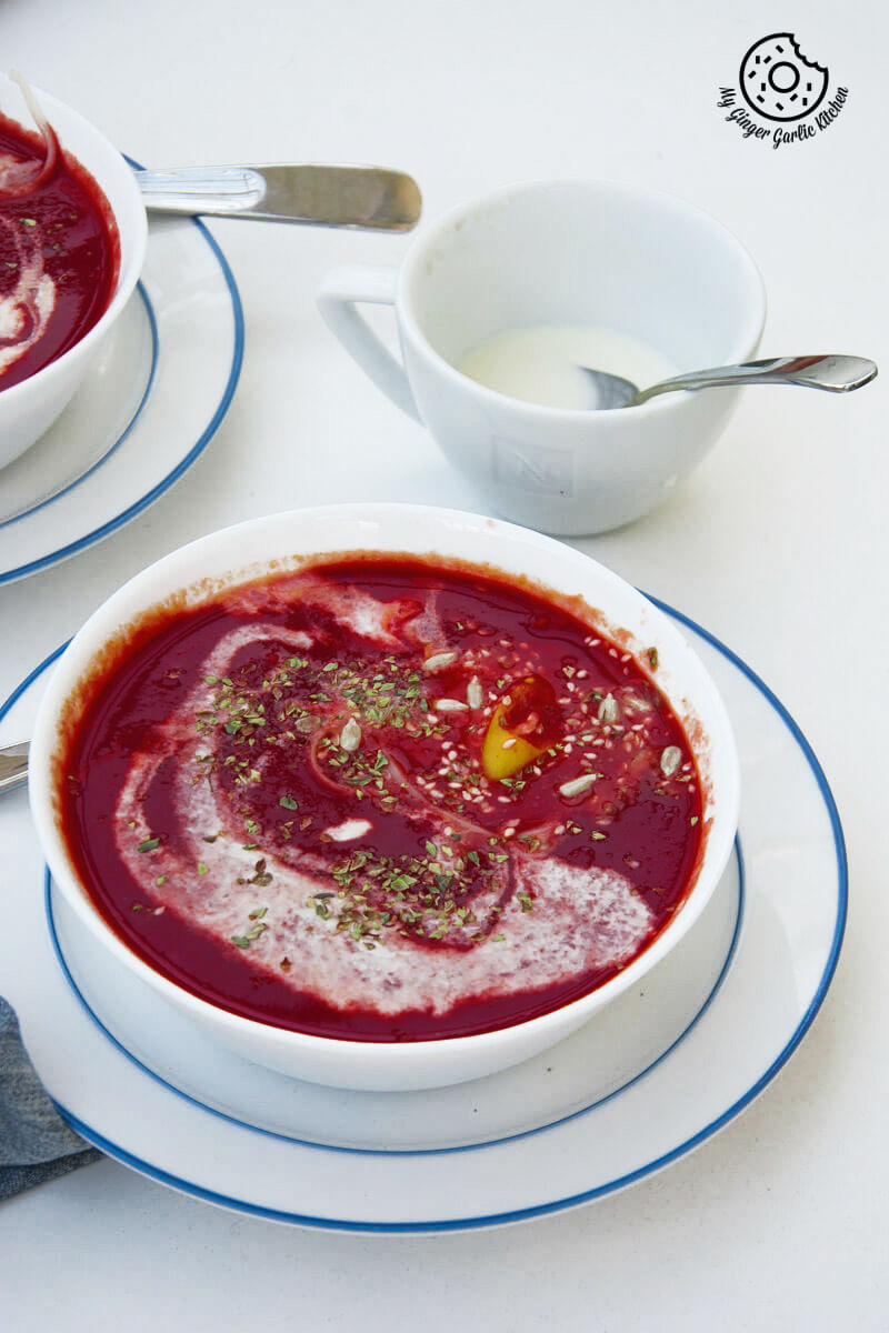 there are two bowls of beet tomato soup on a table with with a cup of cream