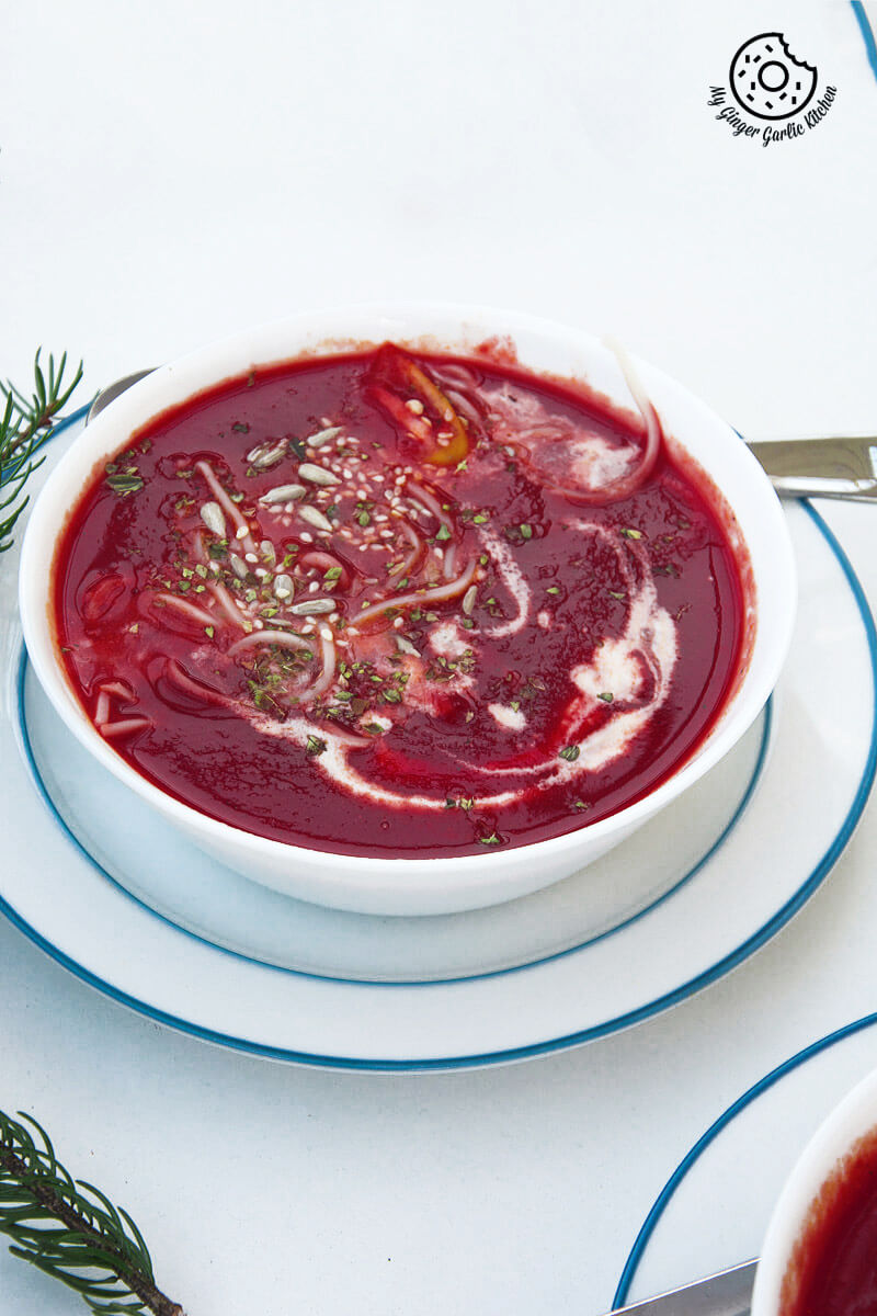 a bowl of beet tomato soup on a table with with a cup of cream