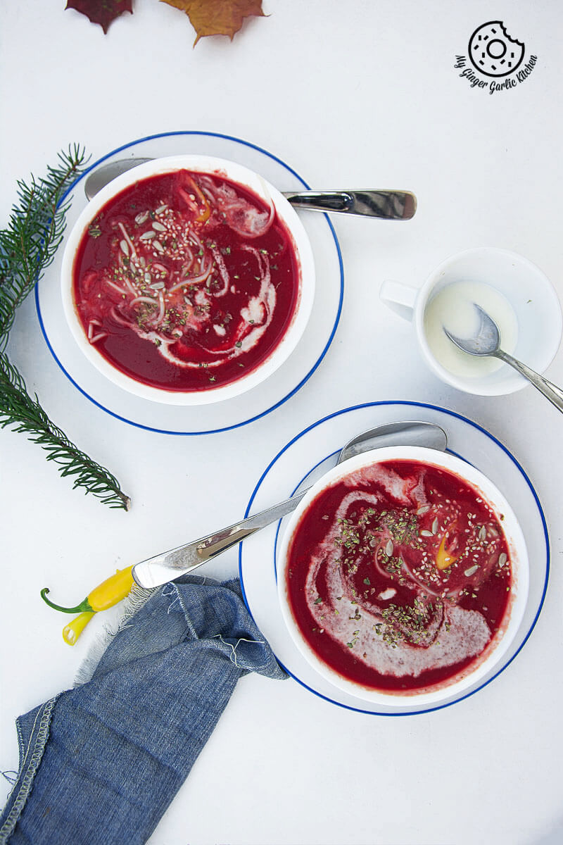 two bowls of beet tomato soup on a table with with a cup of cream