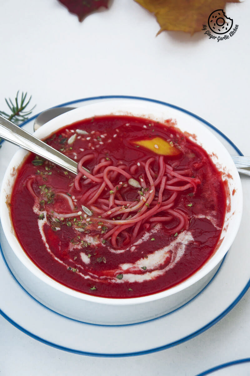 a bowl of beet tomato soup with noodles and a spoon on a plate