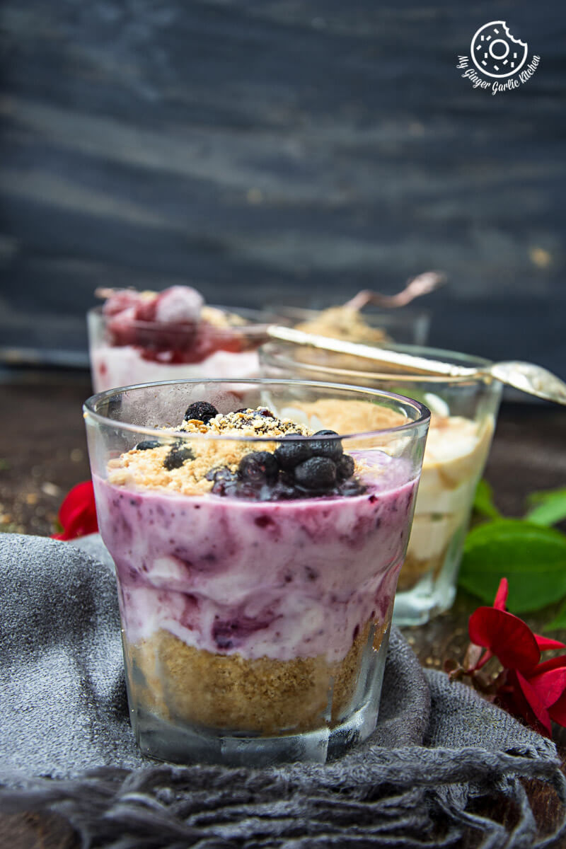 four glasses of different cheesecake shots with berries and granola with a cloth on a table