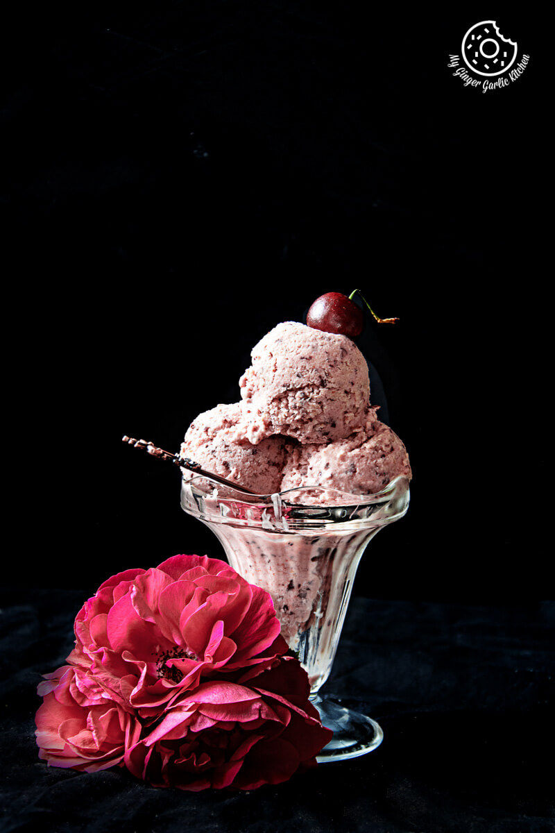 a glass bowl with cherry lassi ice cream and a flower