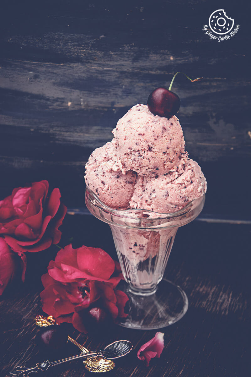 a glass bowl with a cherry lassi ice cream and a cherry on top