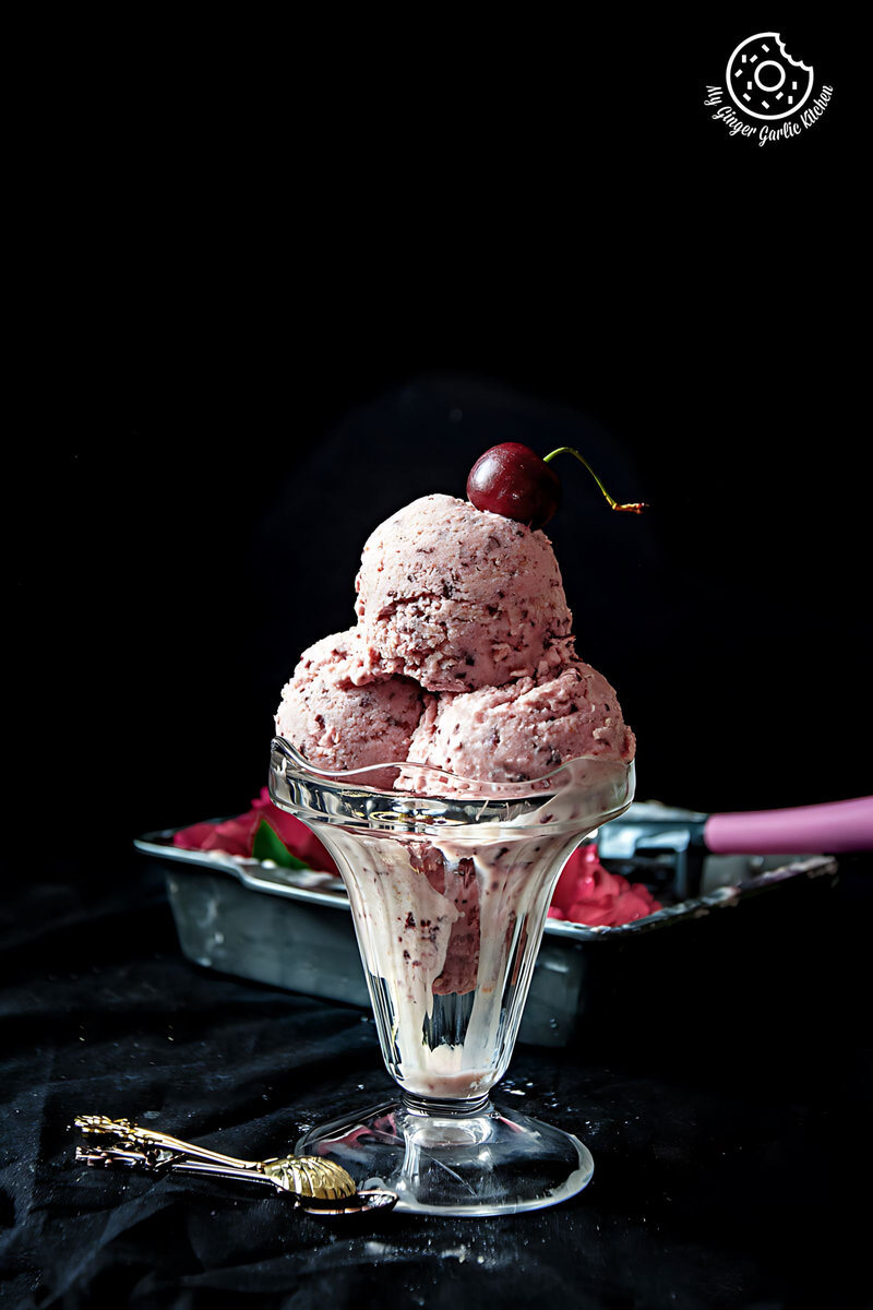 a glass bowl with cherry lassi ice cream and a cherry on top
