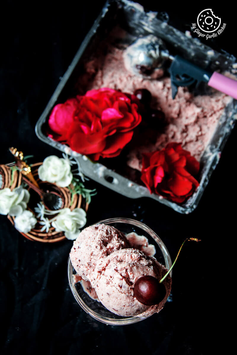 a bowl of cherry lassi ice cream with cherries and a container with ice cream
