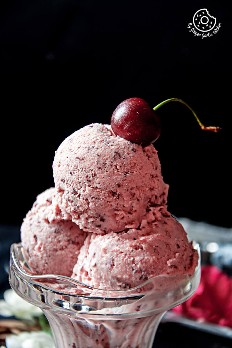 a glass bowl with three scoops of cherry lassi ice cream and a cherry on top