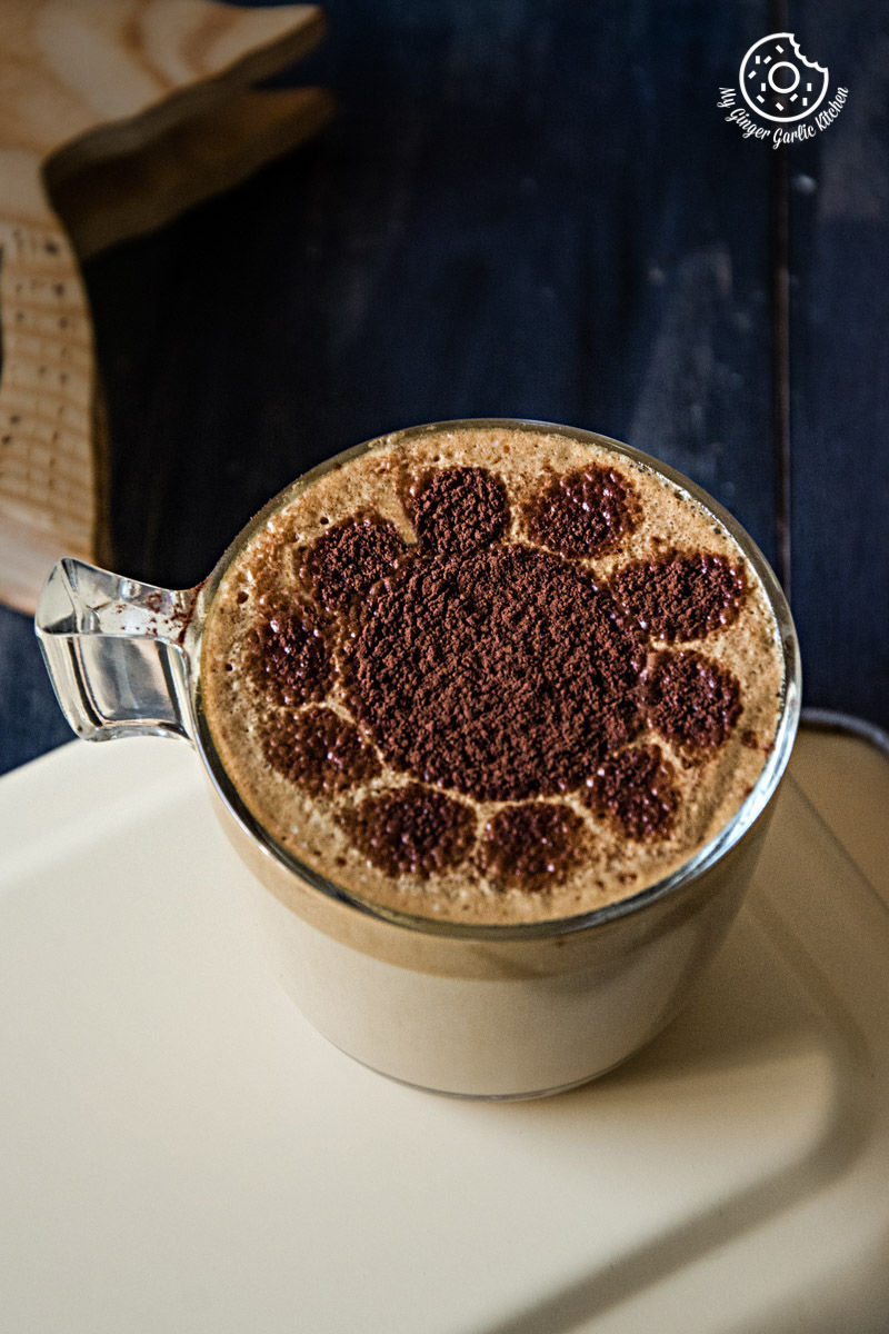 a cup of chocolate almond milk with frothy coffee with cocoa powder design in it
