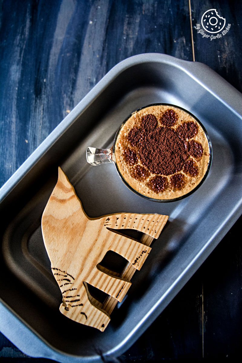 a pan with a chocolate almond milk with frothy coffee and a wooden decoration on it