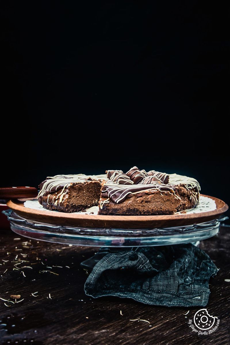 a chocolate cheesecake on a cake stand with a piece missing