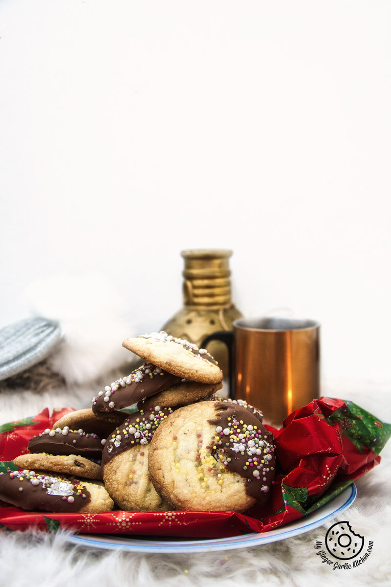 a stack of chocolate dipped whipped shortbread cranberry cookies and a cup of coffee on a table