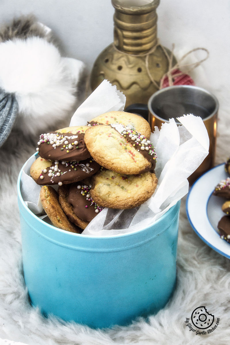 a few chocolate dipped whipped shortbread cranberry cookies in a cookie tin on a table