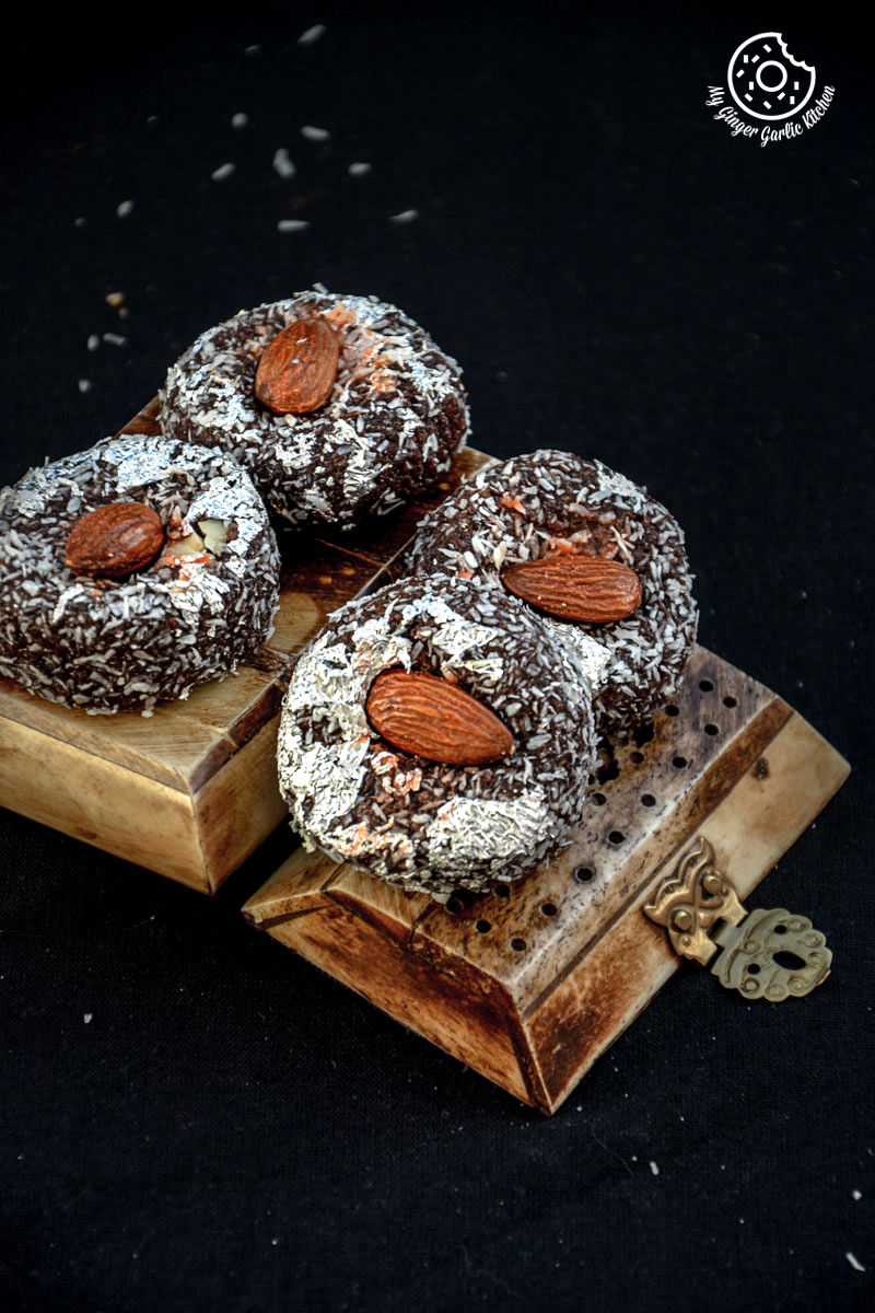 four chocolate coconut delights topped with almonds on a wooden board