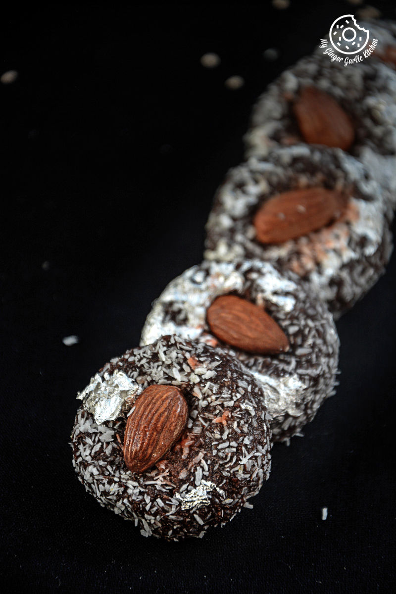 four chocolate coconut delights topped with almonds on a black surface