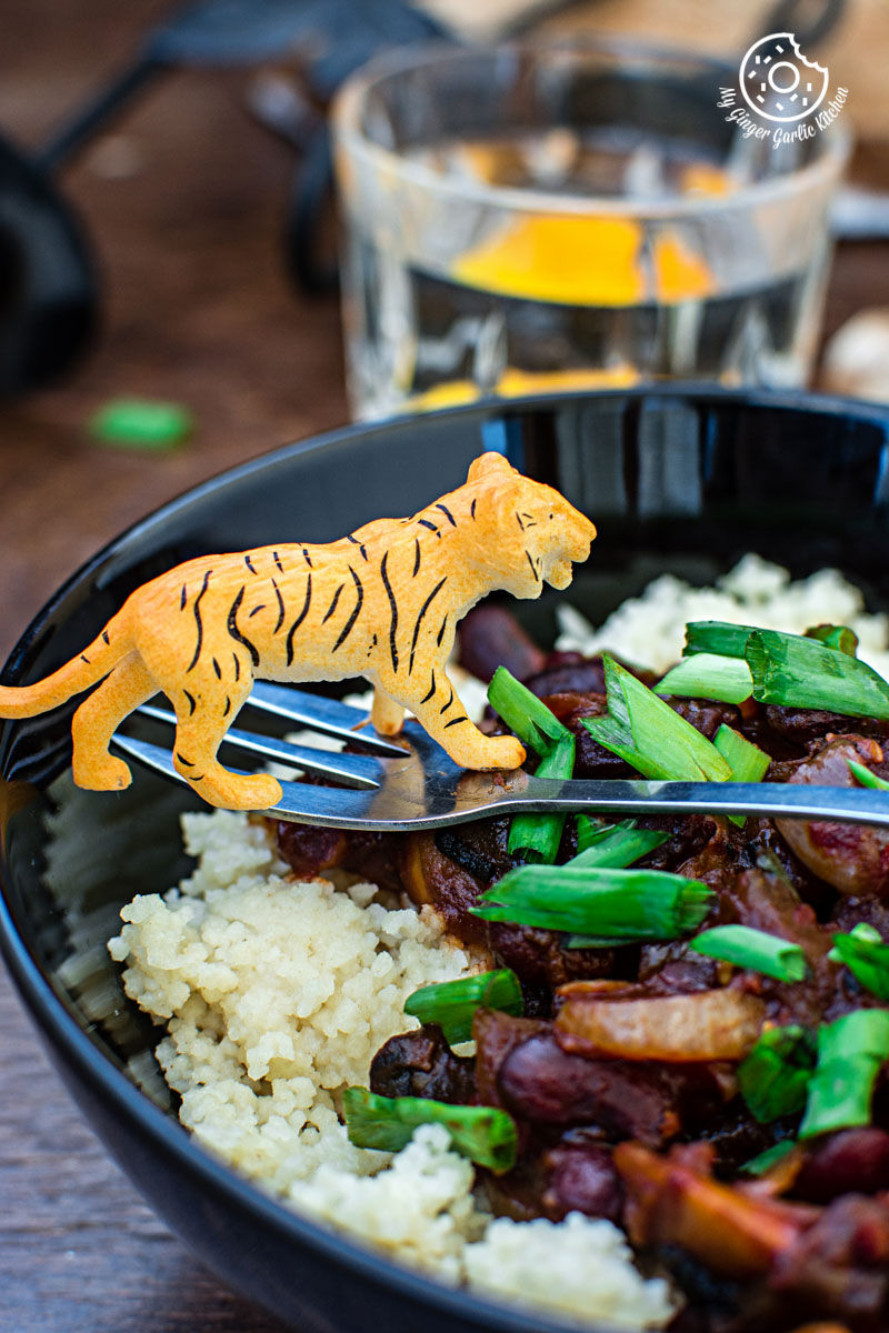 a bowl of couscous with sauteed mushrooms and kidney beans and a toy tiger on it