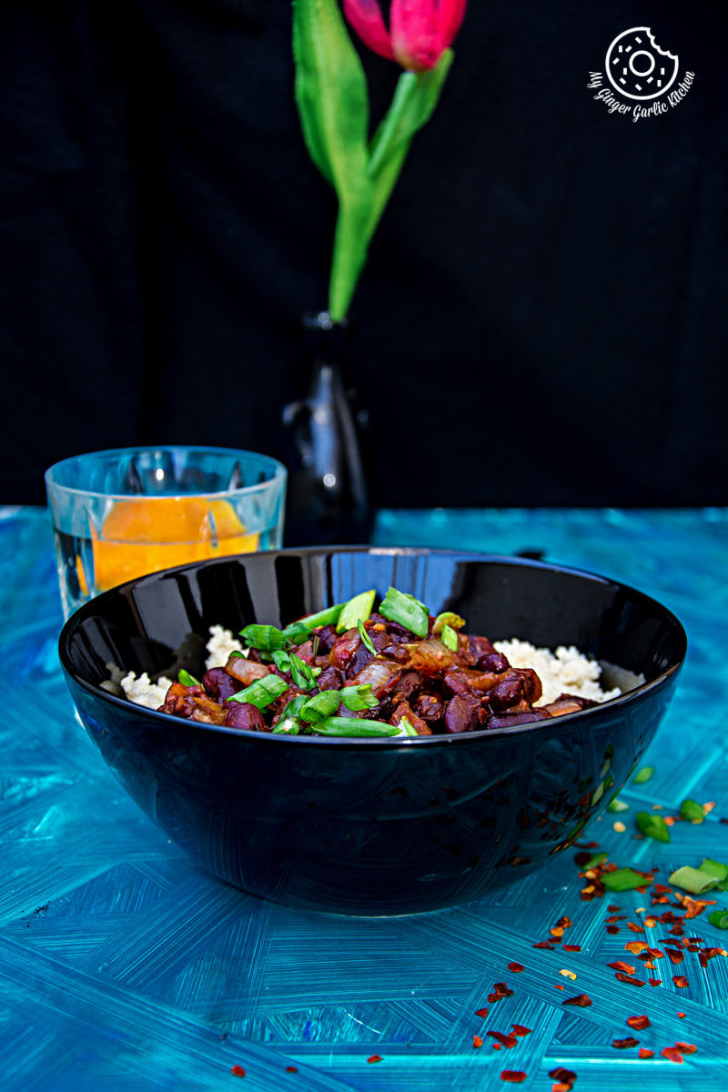 a bowl of couscous with sauteed mushrooms and kidney beans with a glass of water on a table with a vase of flowers