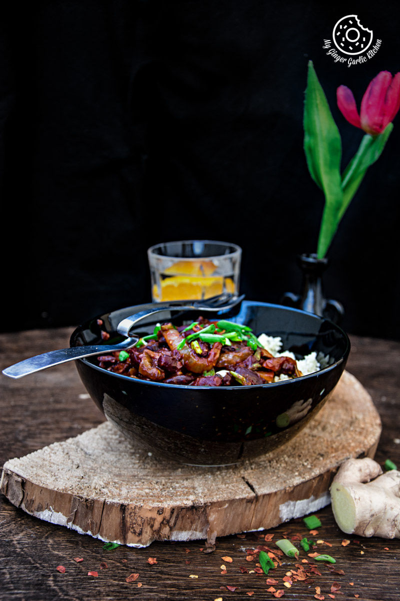 a bowl of couscous with sauteed mushrooms and kidney beans on a wooden table with a flower