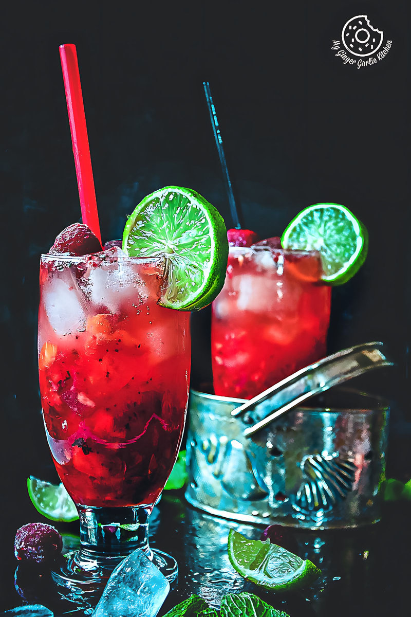 there are two glasses of dark rum strawberry mango mojito cocktails with lime wedges and strawberries