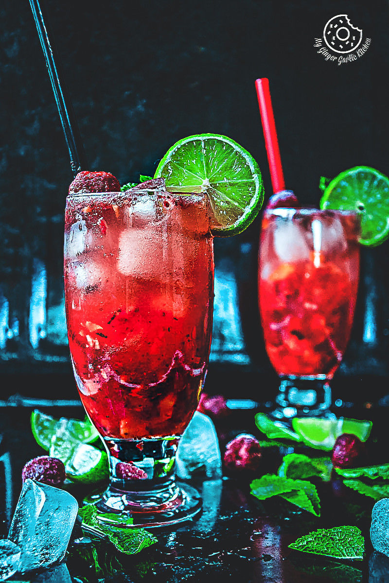 there are two glasses of dark rum strawberry mango mojito with ice and lime on the table