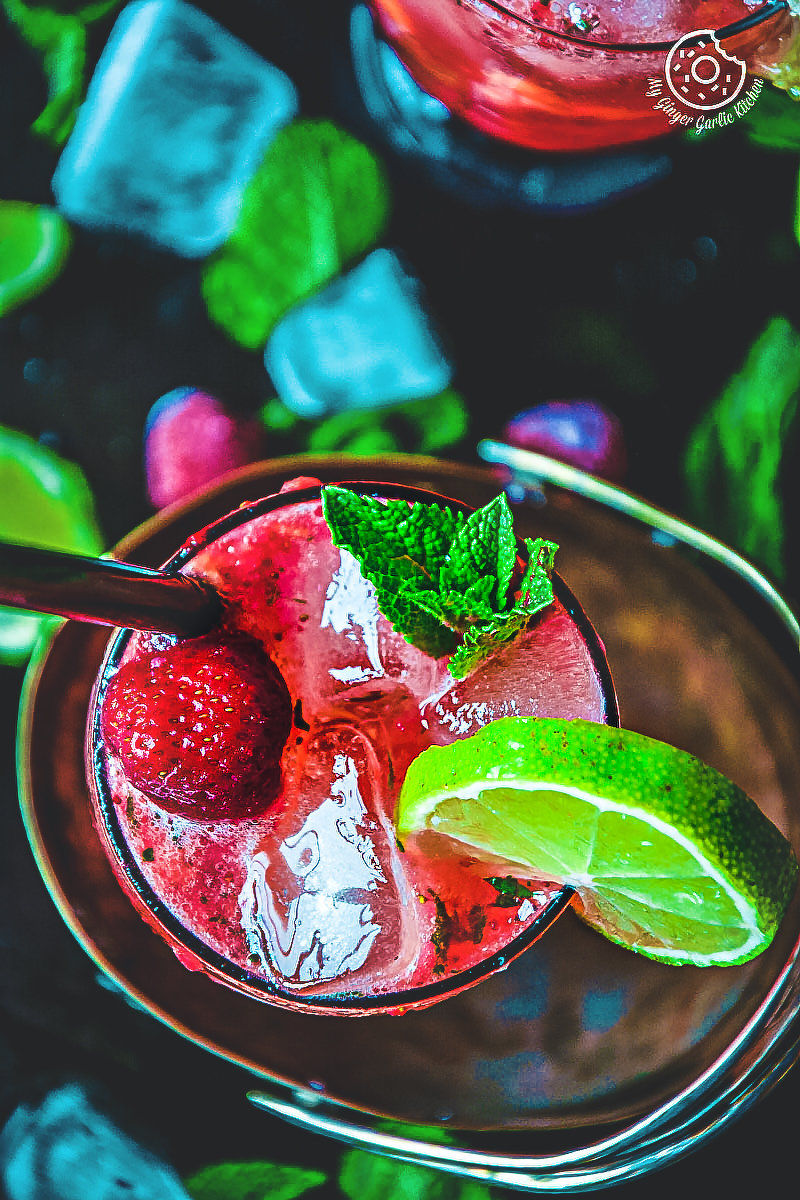 there is a close up of a dark rum strawberry mango mojito with a strawberries and lime