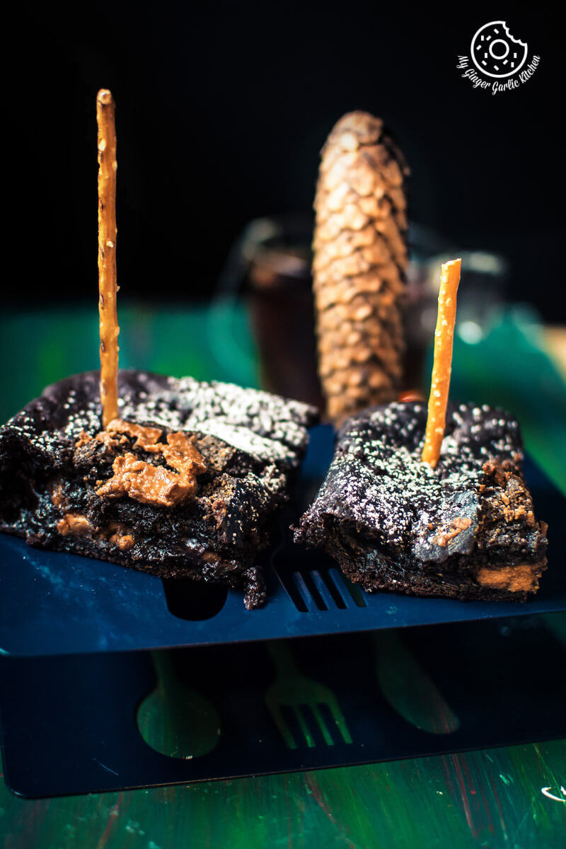 two eggless banana peanut butter chocolate brownies on a blue plate with a pinecone in background