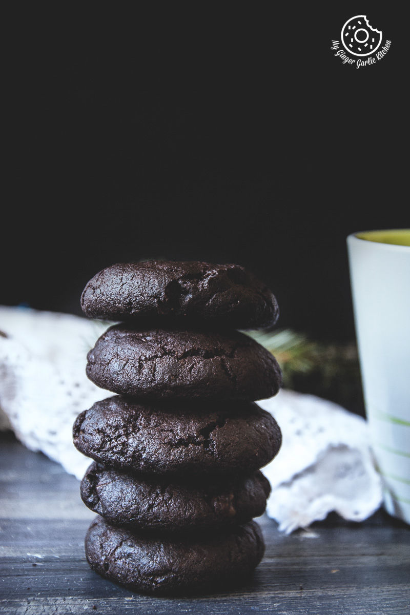 a stack of eggless triple chocolate cookies on a table next to a cup