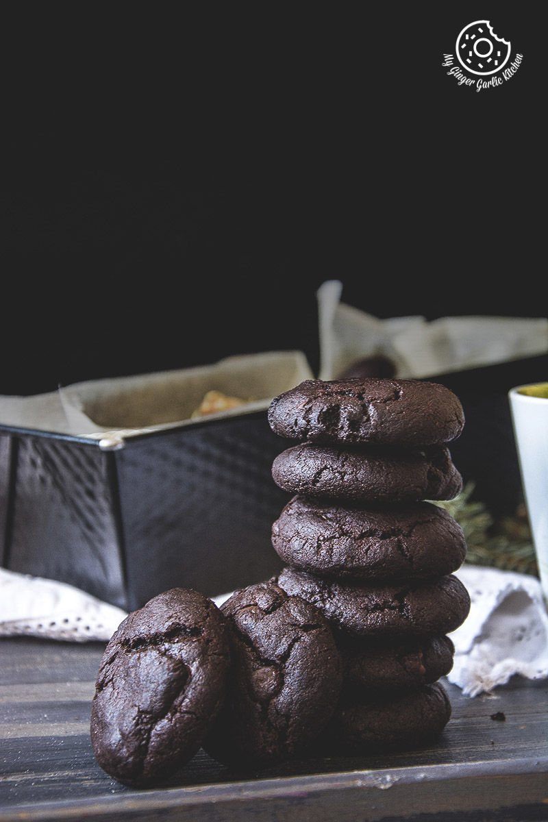 a stack of eggless triple chocolate cookies on a table next to a cup of coffee