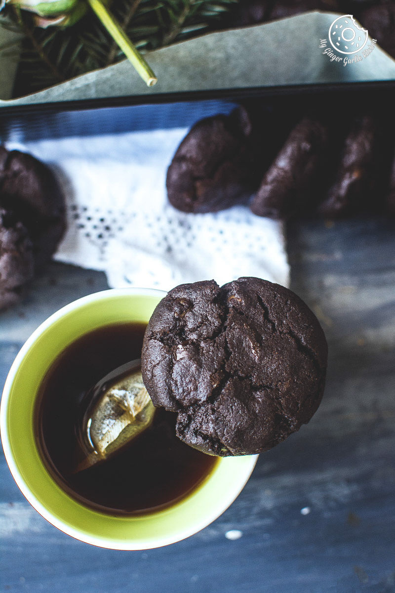 a cup of tea and a eggless triple chocolate cookie on top of it with some more cookies a table