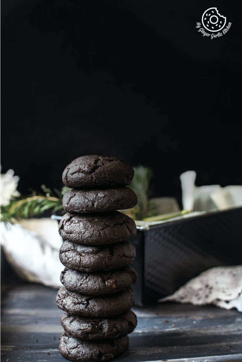 a stack of eggless triple chocolate cookies on a table with a bowl of flowers