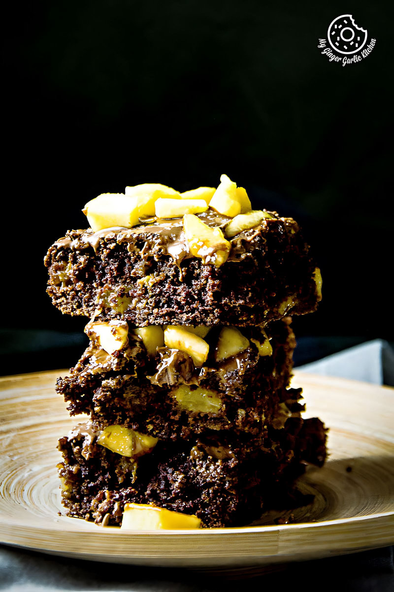 a stack of eggless peach brownies with peaches and icing sugar on top on a plate
