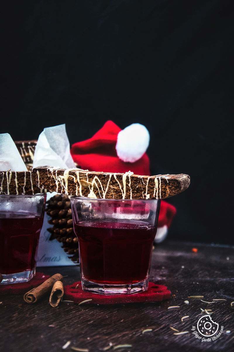 there are two glasses of red wine with Gingerbread Biscotti and a santa hat