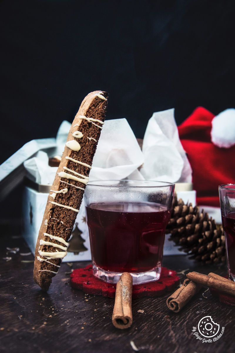 there is a Gingerbread Biscotti With White Chocolate Drizzle and a glass of wine on a table