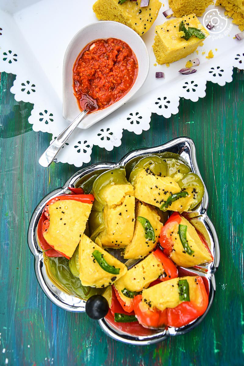 a plate of gujarati khaman dhokla cooked in a bell peer with a bowl of sauce
