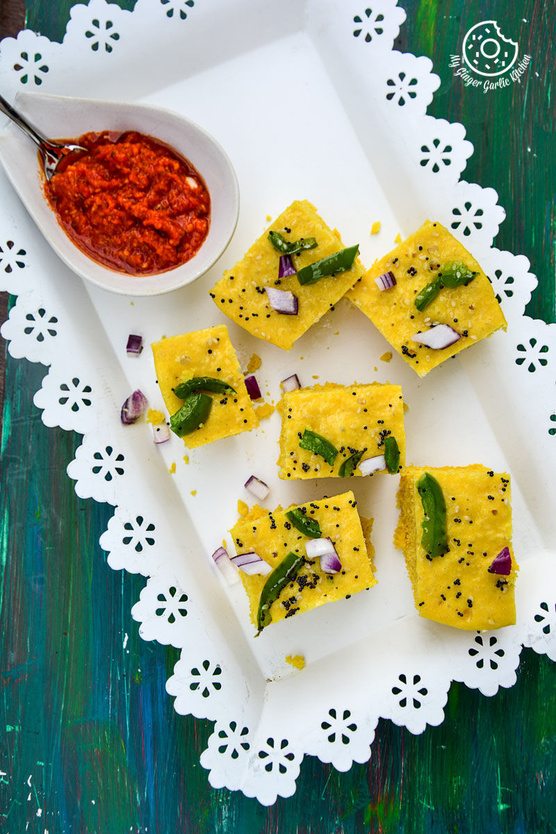 a plate of gujarati khaman dhokla wit a bowl of red chutney