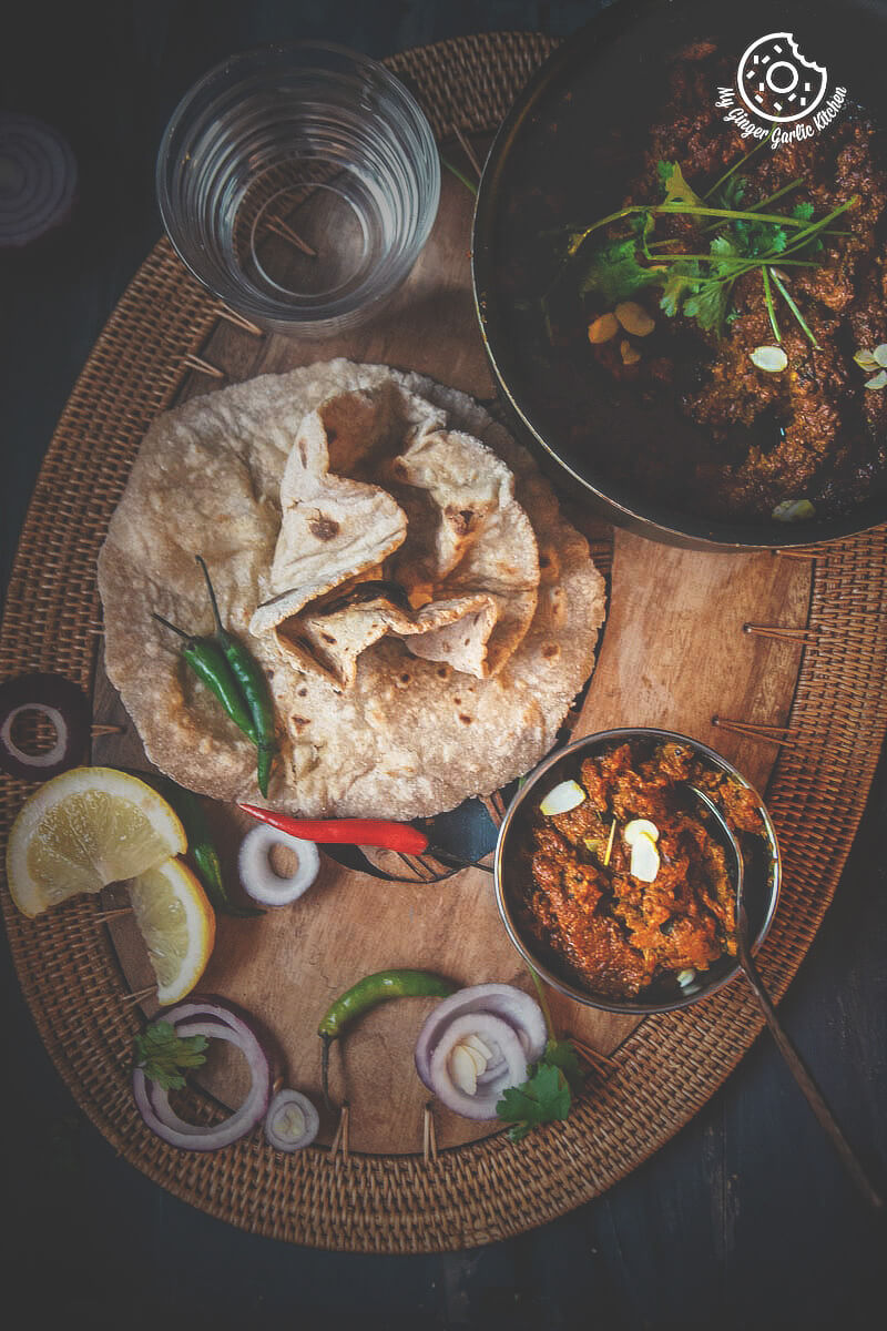a plate of rajasthani haldi ki sabji with roti, salad, and pan of sabji on a wooden plate