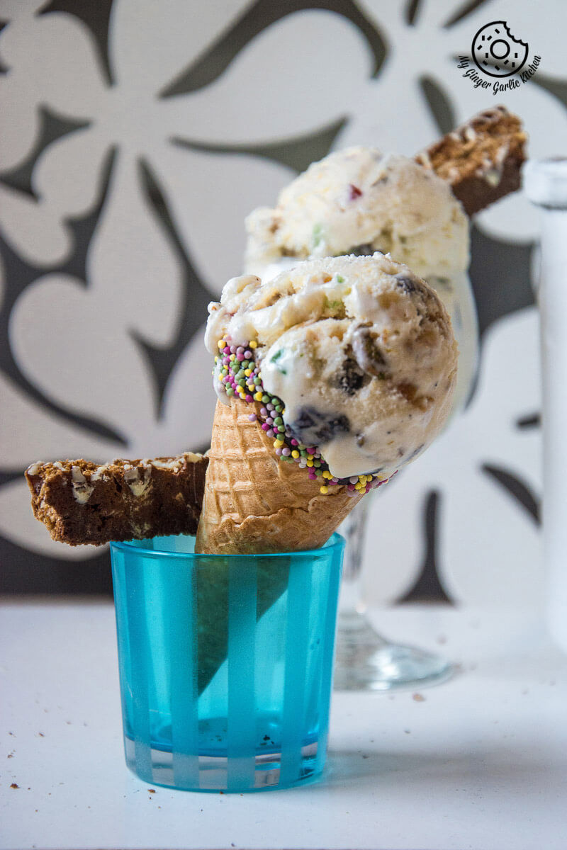 a ice cream cone with holiday fruit and nut ice cream and sprinkles in a blue cup