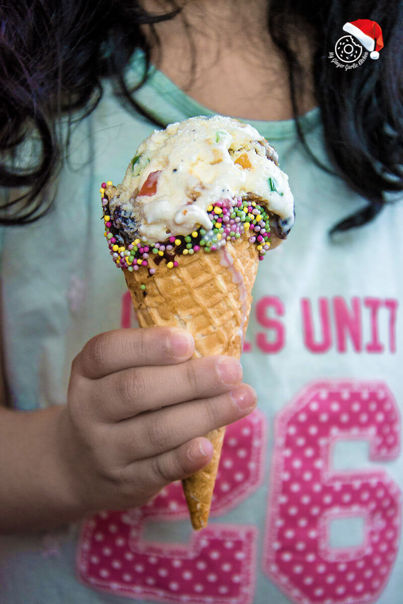 a girl holding a cone of holiday fruit and nut ice cream with sprinkles
