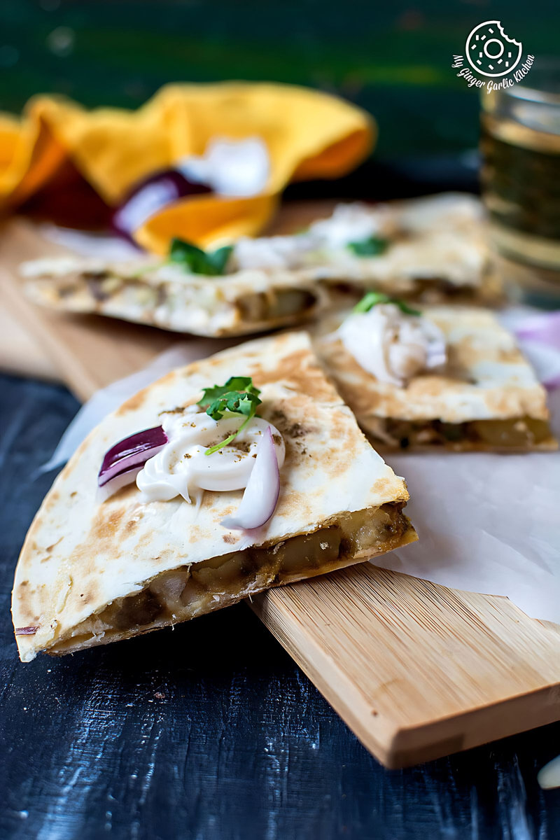 two jeera aloo quesadillas on a cutting board with a glass of beer