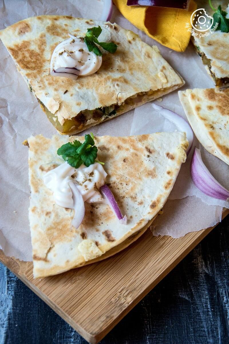 four pieces of jeera aloo quesadilla on a cutting board with onions