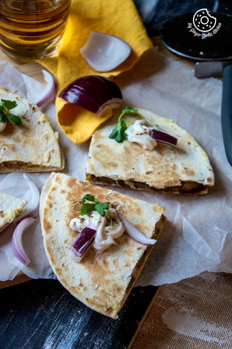 four pieces of jeera aloo quesadilla with onions and cheese on a table