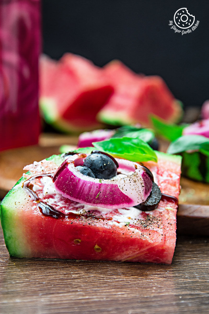 a slice of juicy watermelon pizza with basil and blueberry on it