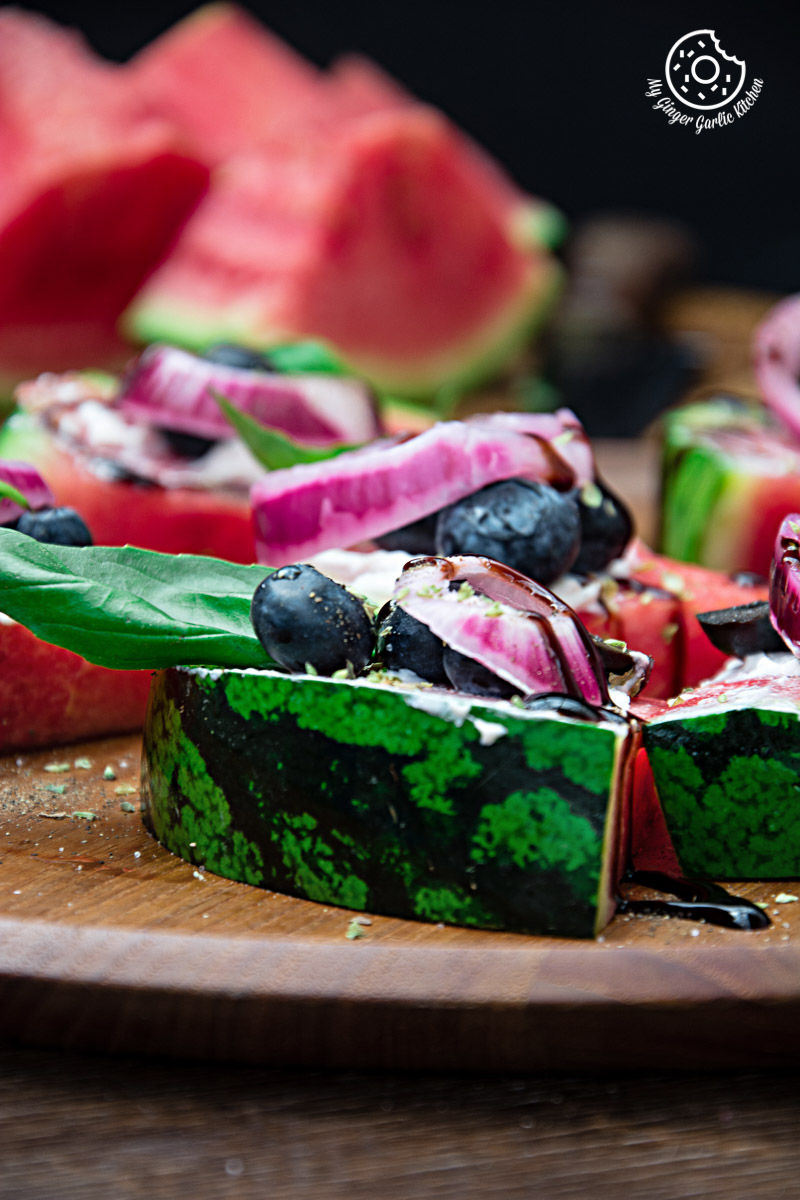 slices of juicy watermelon pizza bites with blueberries and onions on a cutting board