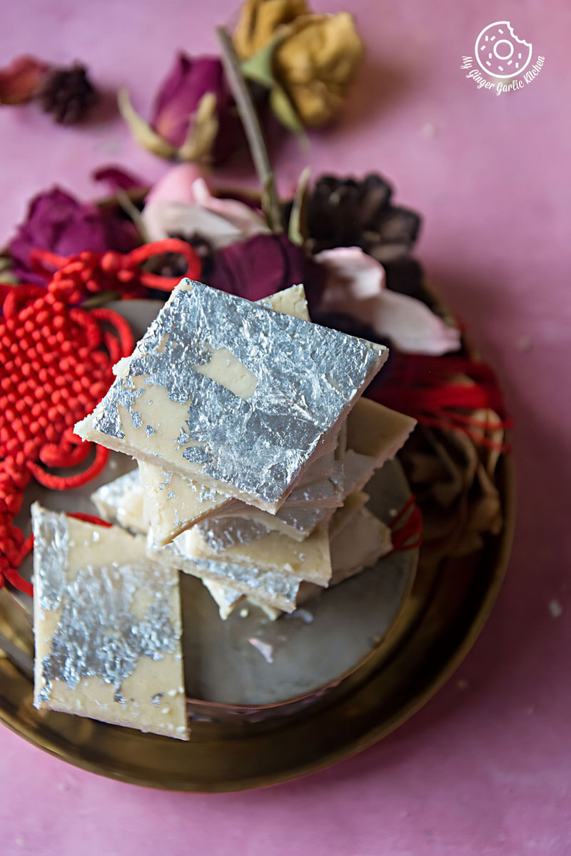 a stack of kaju katli with dried flowers on a pink table