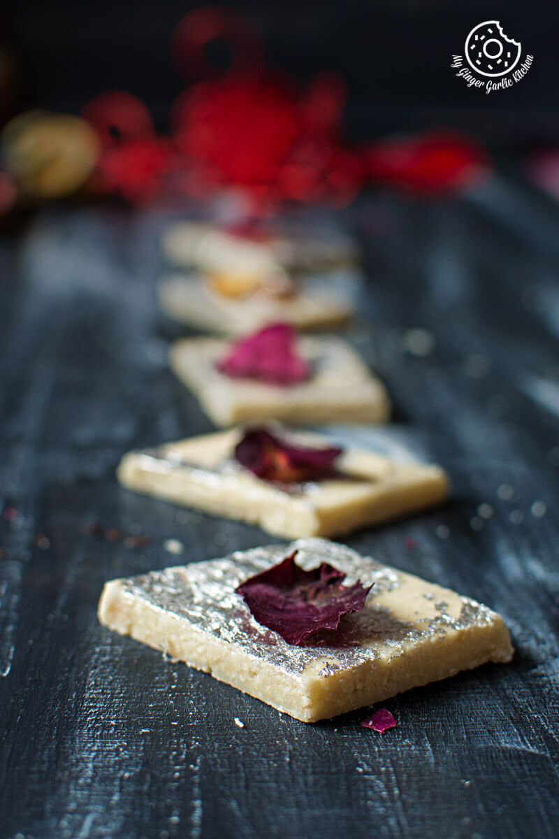 some kaju katli on a table dried red rose petals