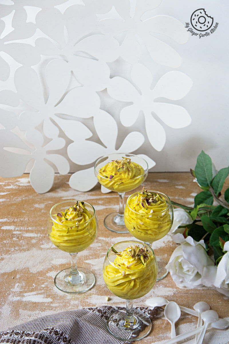 four kesar elaichi shrikhand desserts in small glasses on a table
