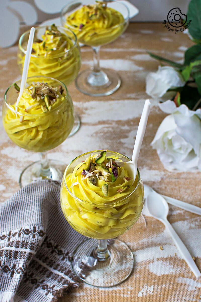 three glasses of kesar ilaichi shrikhand dessert with a white spoon and a napkin