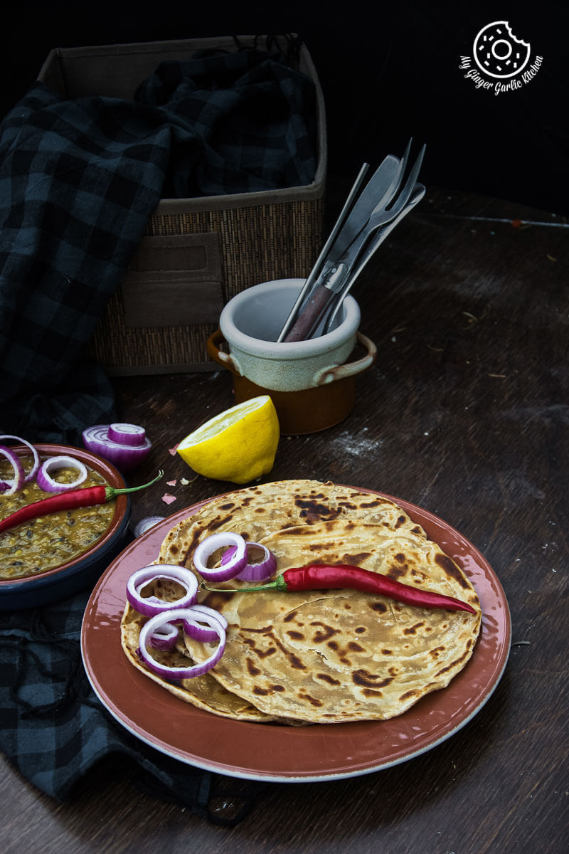 there are two plates of three lachha parathas on a table with a bowl of lemons